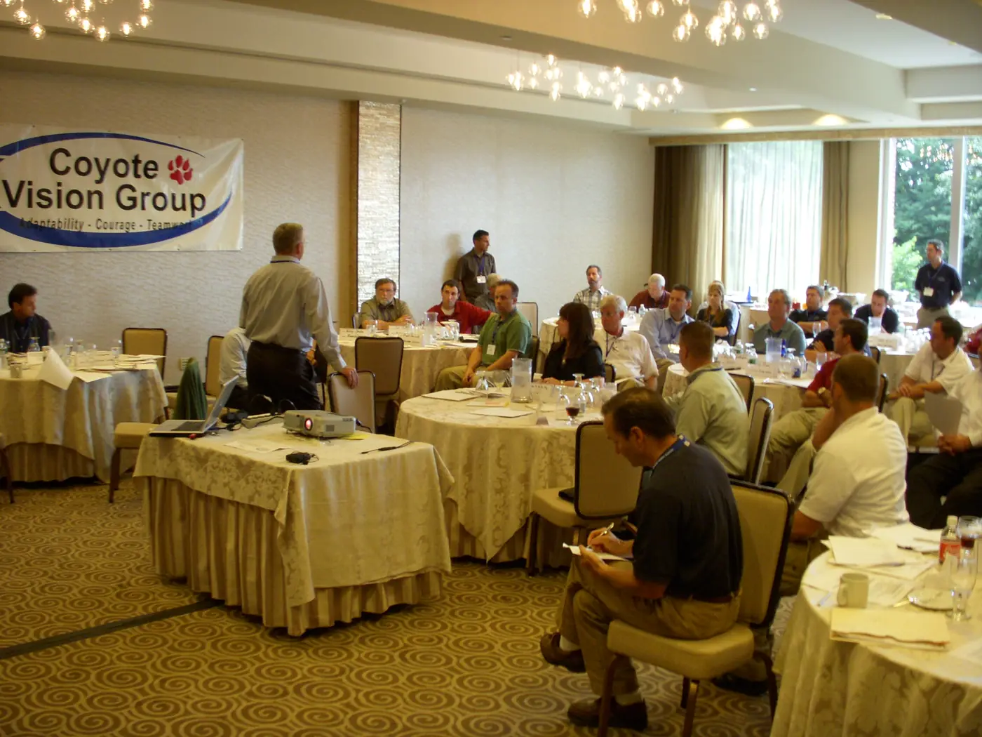 Wide view of a Coyote Vision Group conference room with attendees at tables below the branded banner