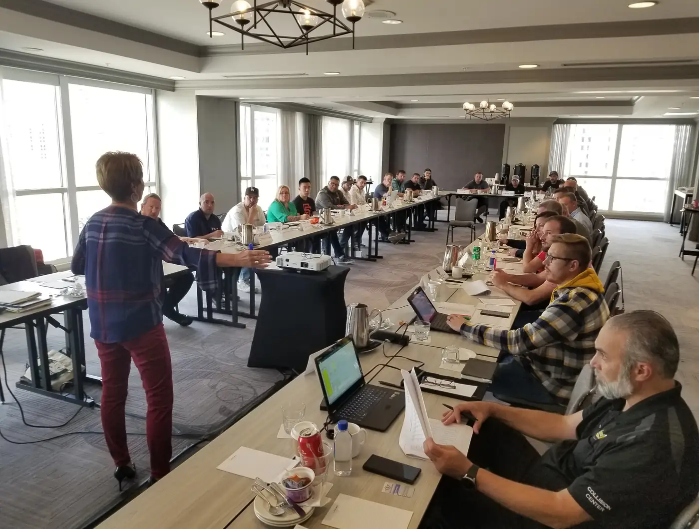 A presenter addressing attendees seated at U-shaped tables during an industry training session